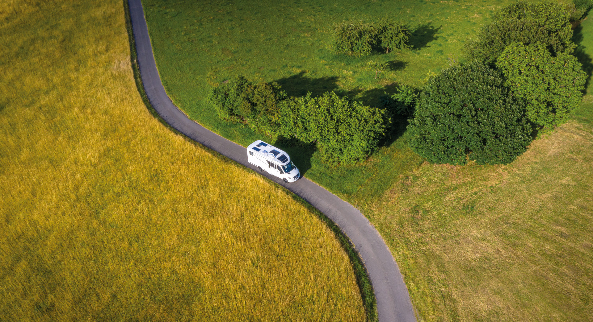 Wohnmobil fährt s-förmige Landstraße zwischen Wiesenlandschaften