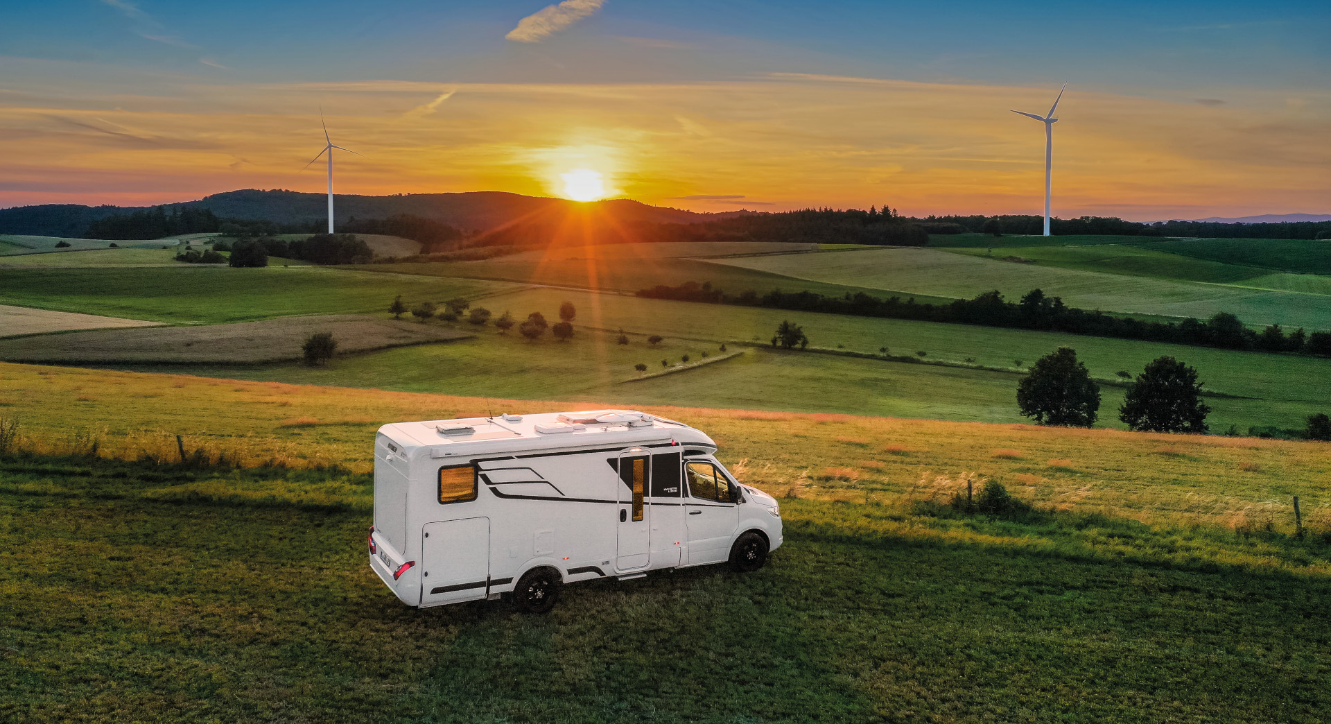 Wohnmobil steht auf einer Wiesenlandschaft und die Sonne geht unter